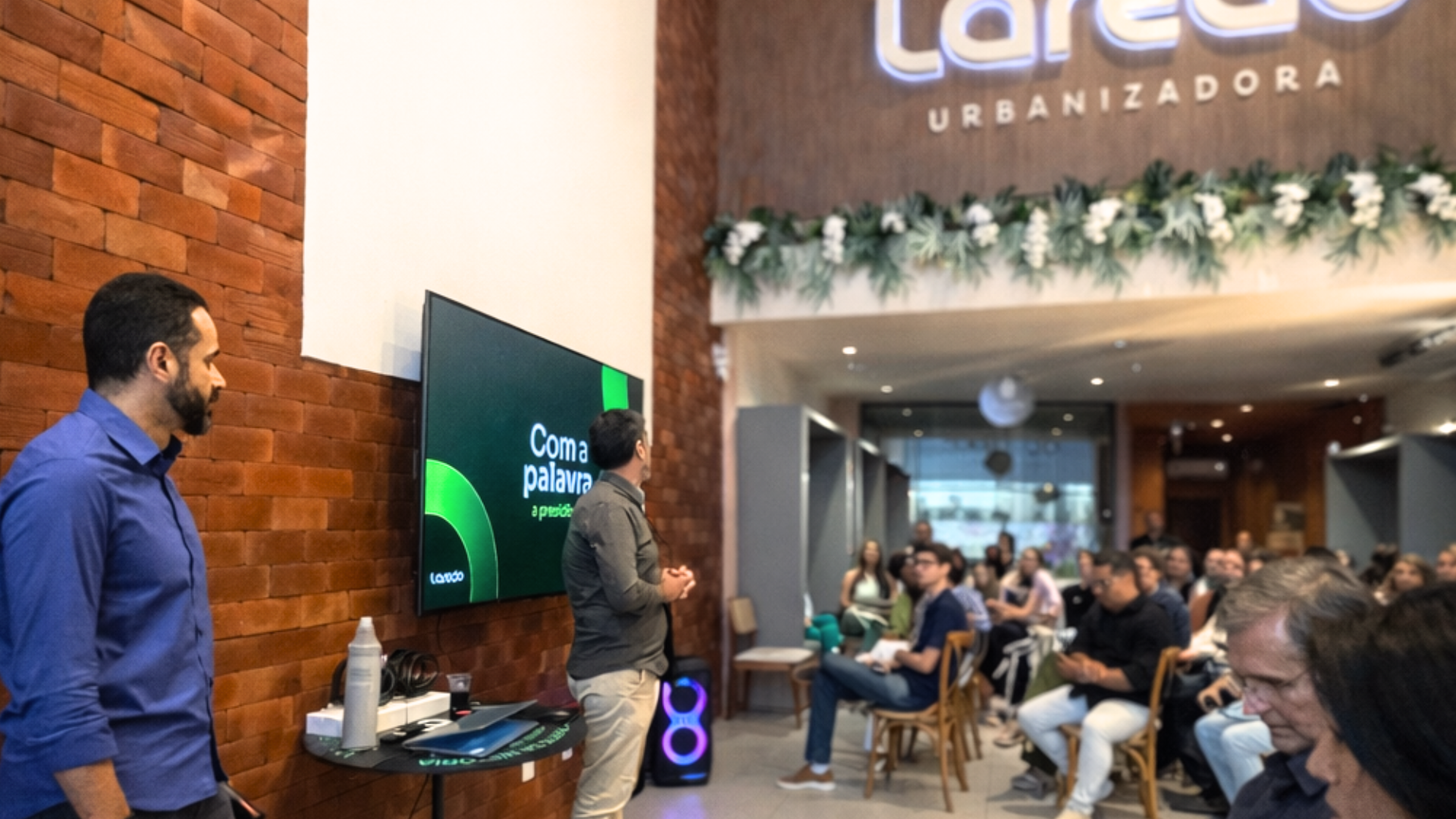 dois homens em frente a uma tv com a marca laredo urbanizadora no canto superior direito